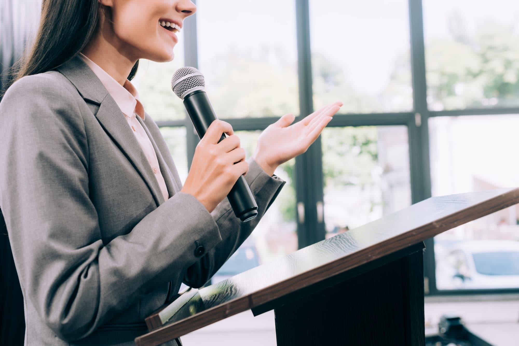 cropped image of smiling lecturer talking into microphone and gesturing at podium tribune during
