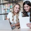 smiling young businesswomen using digital devices at workplace