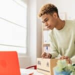 Young adult man copying costumer address from email on package before sending