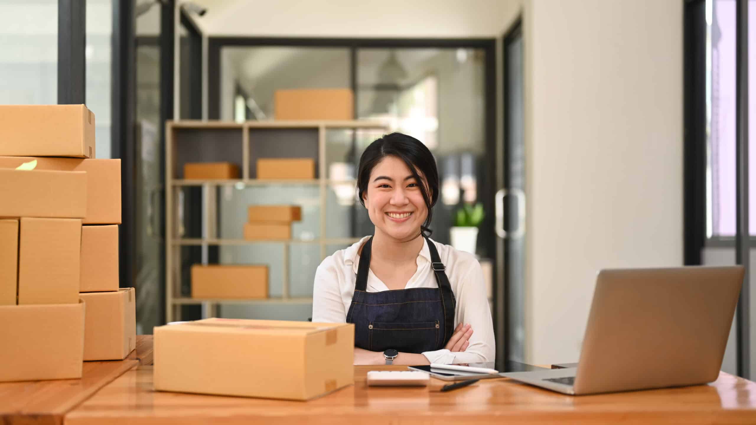 Confident young female small business entrepreneur sitting with arms crossed and smiling at camera.