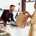 Shop assistant handling shopping bag to female customer in grocery store