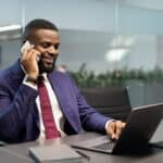 Successful african american businessman working on laptop, having phone conversation