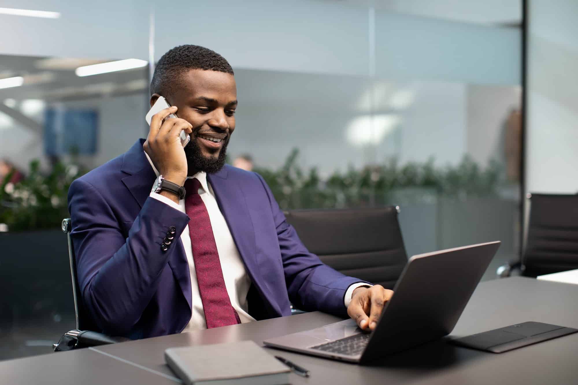 Successful african american businessman working on laptop, having phone conversation