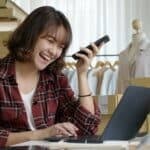 Young asia seller woman happy work on laptop busy cellphone call chat to customer
