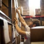 Worker reaching up for cardboard box stored in warehouse