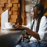 Side view of black lady enjoying morning coffee and checking emails on laptop