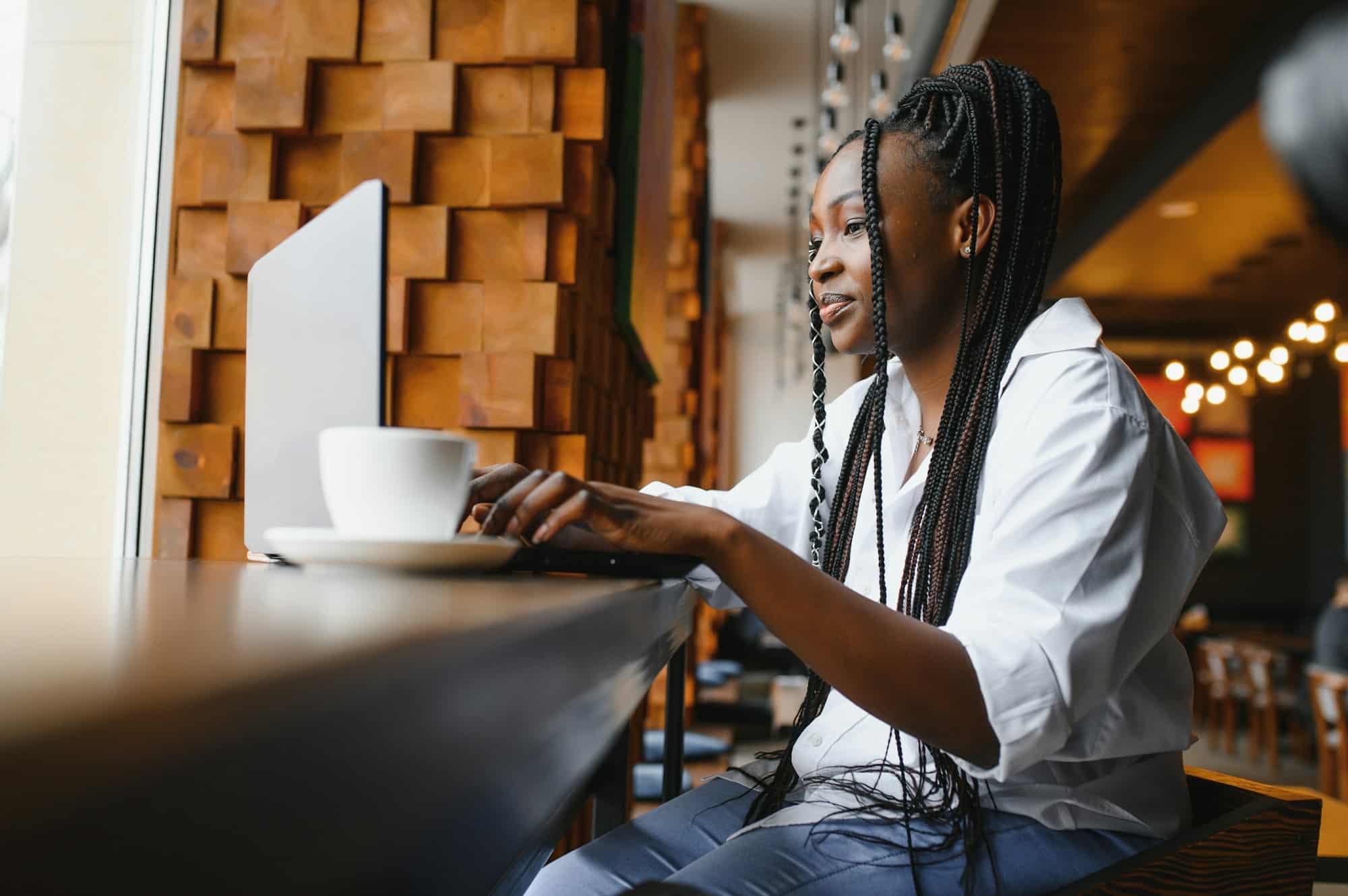 Side view of black lady enjoying morning coffee and checking emails on laptop