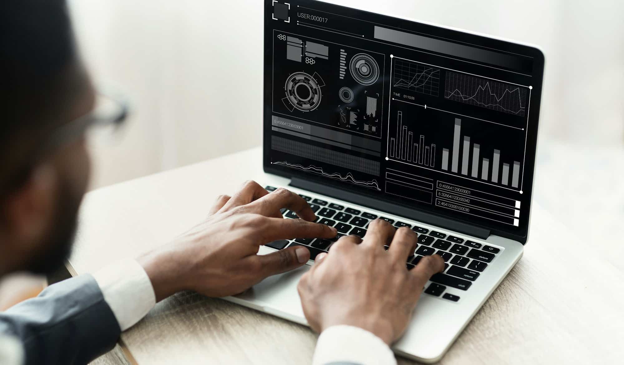 Black Businessman Working On Laptop With Graphs Sitting In Office